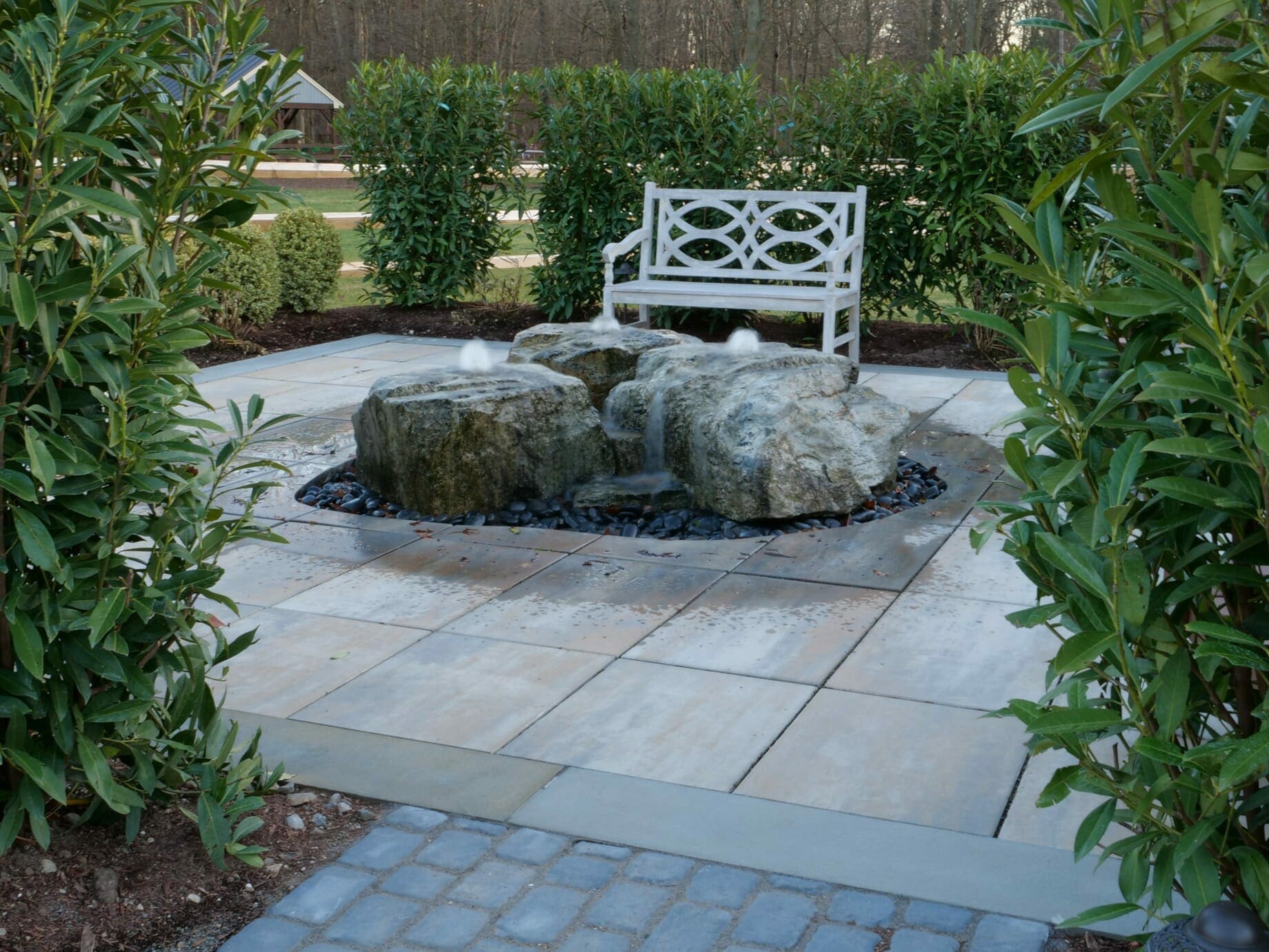 Bubbling rock fountainscape set into a bluestone patio beside a garden bench