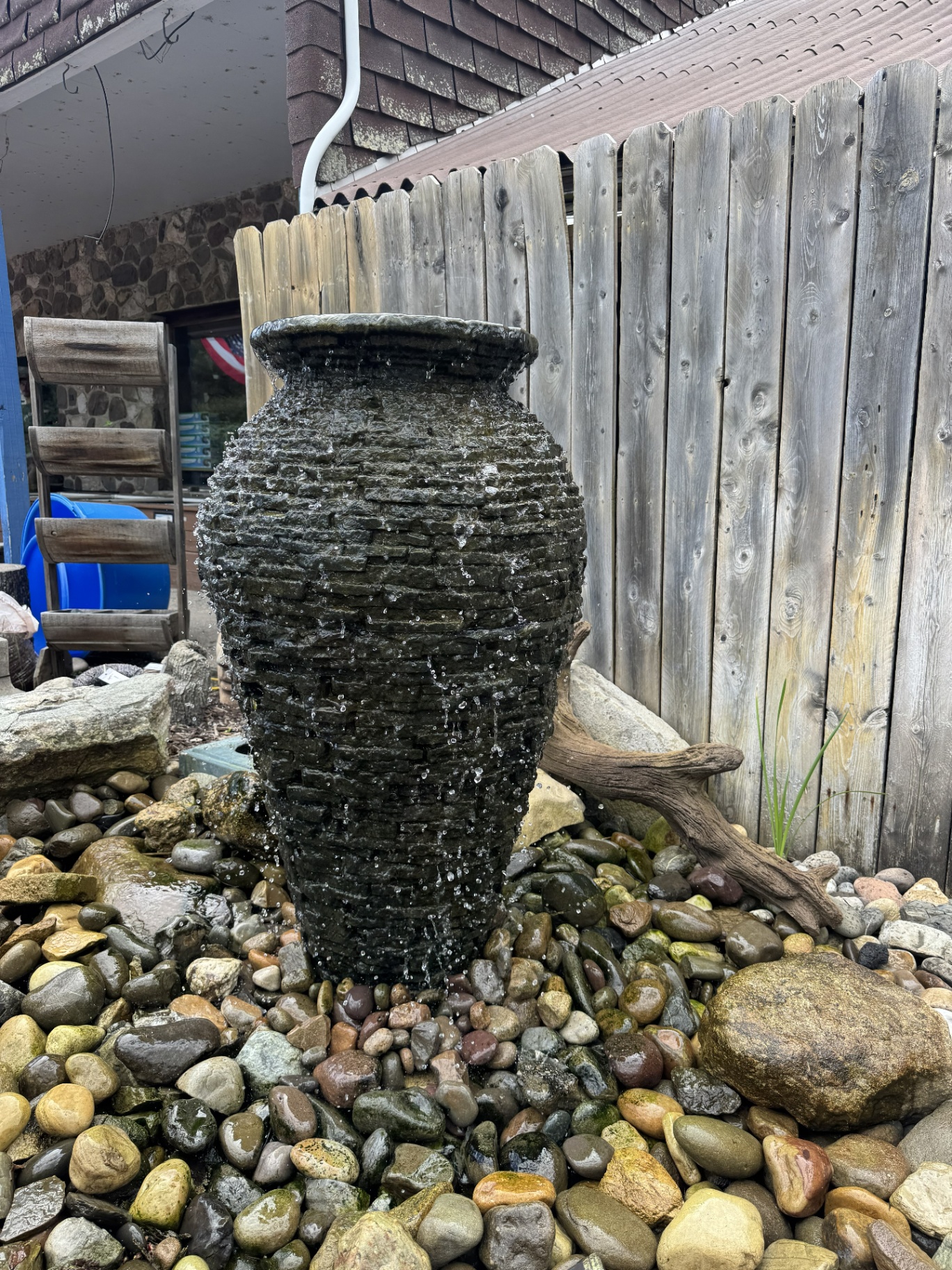 Stacked slate urn fountain on a river rock basin in a backyard garden