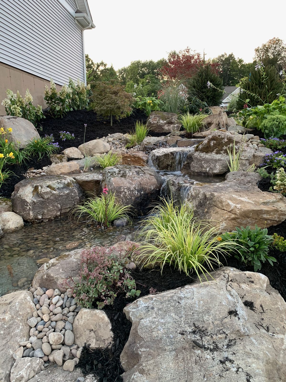 Finished pond waterfall framed by new plantings after a full redesign