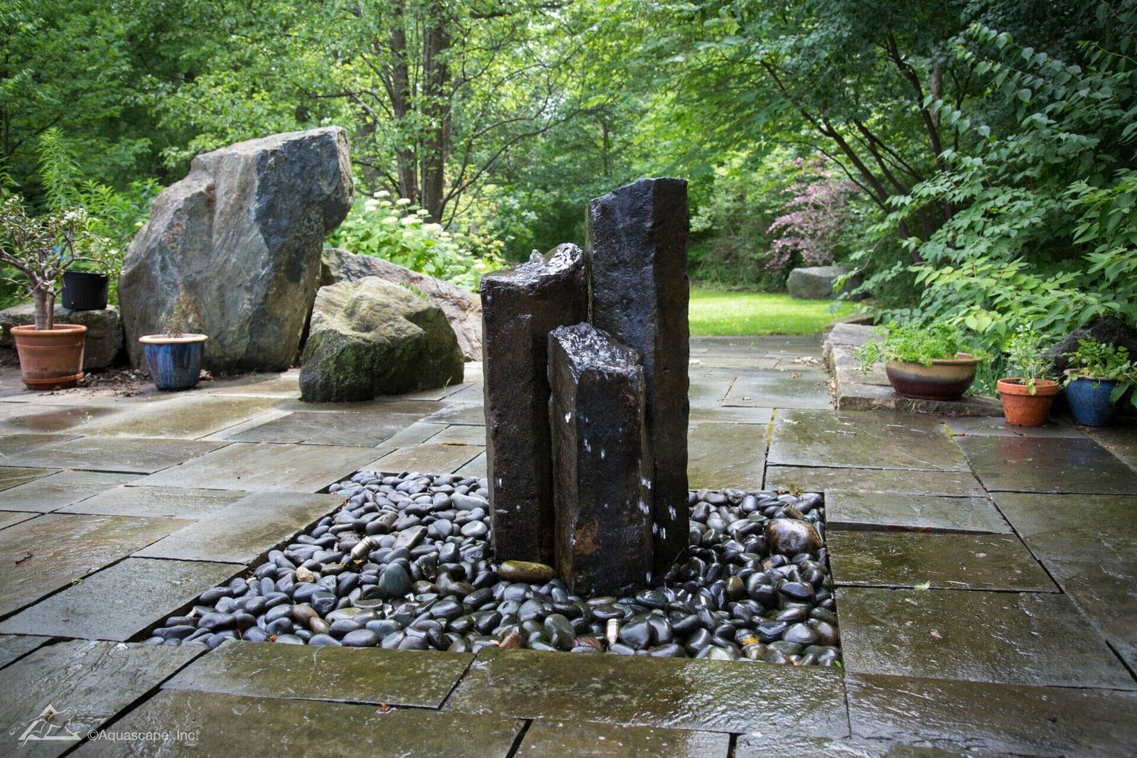 Three Mongolian basalt columns bubbling over polished river rock on a bluestone patio