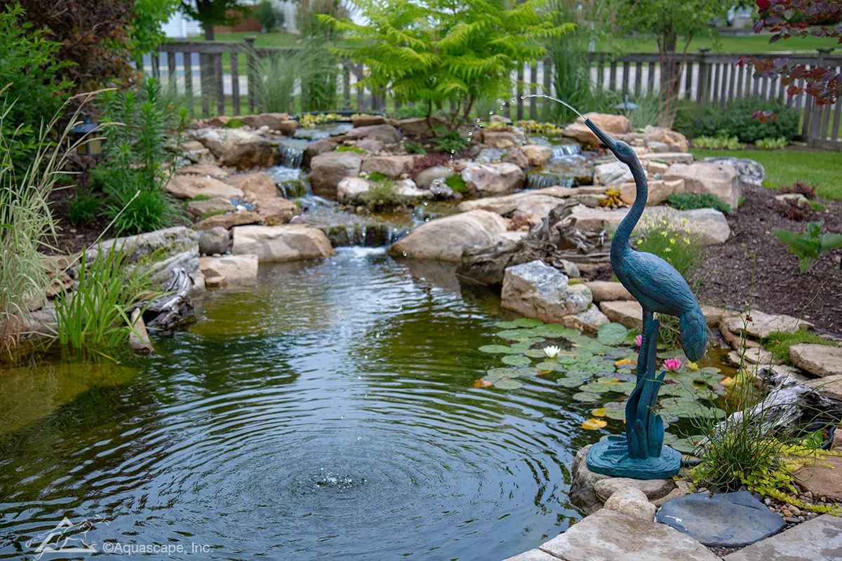 Heron shaped spitter standing at the edge of a backyard pond